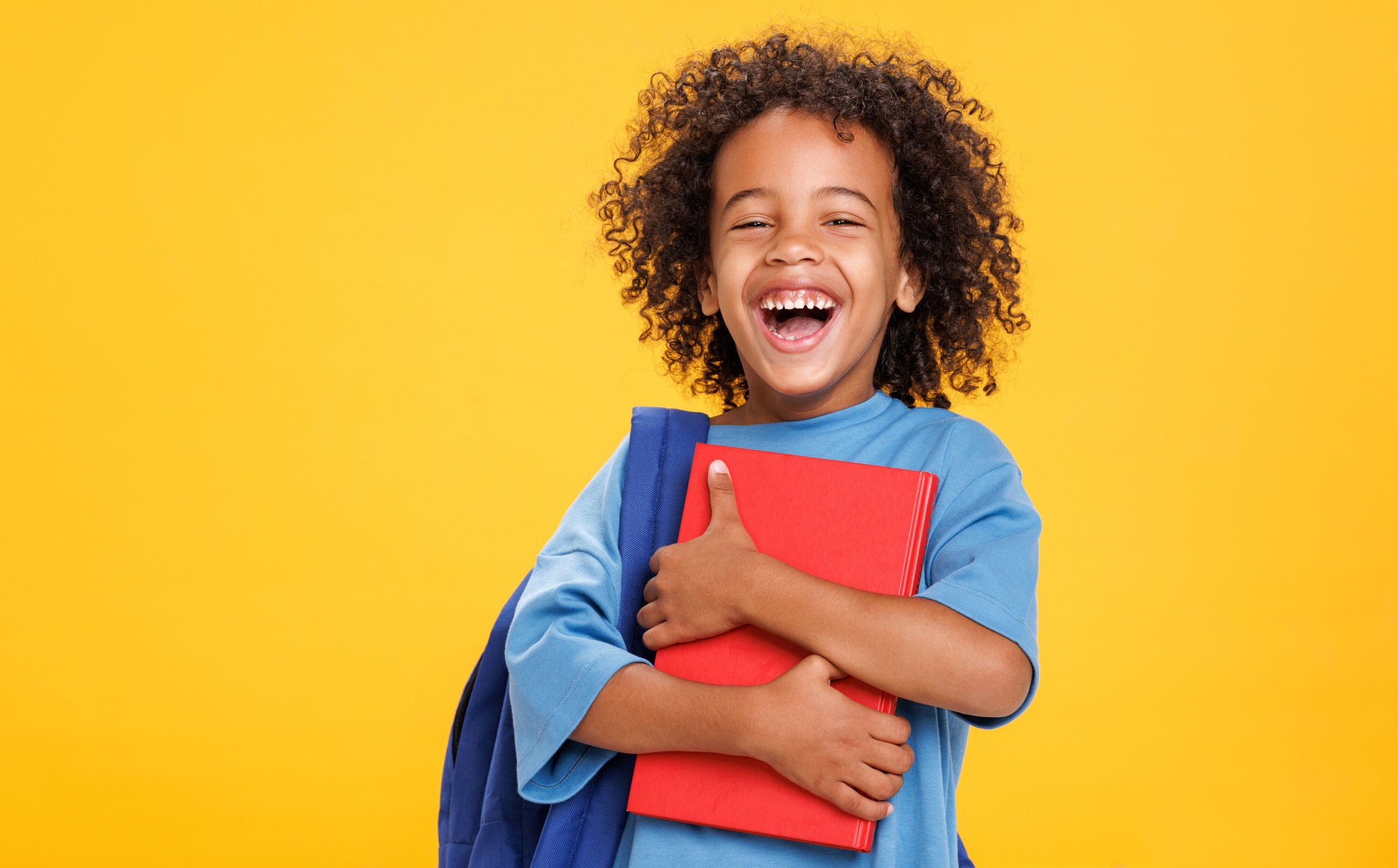 Happy ethnic schoolboy laughing with book