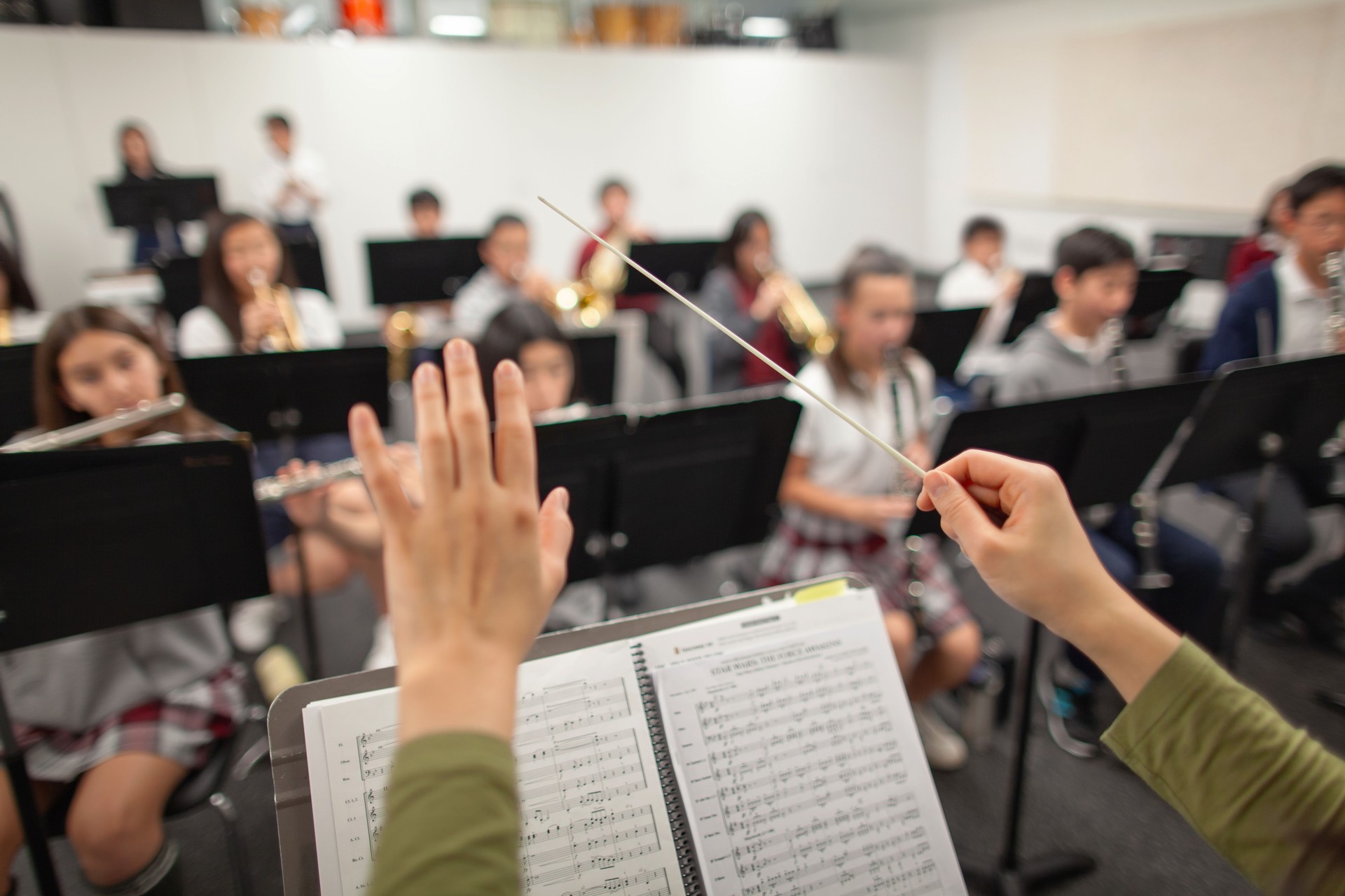View of band instructor teacher conductor hands leading music performance orchestra of junior high school teenager students practicing in school classroom together in a group of people
