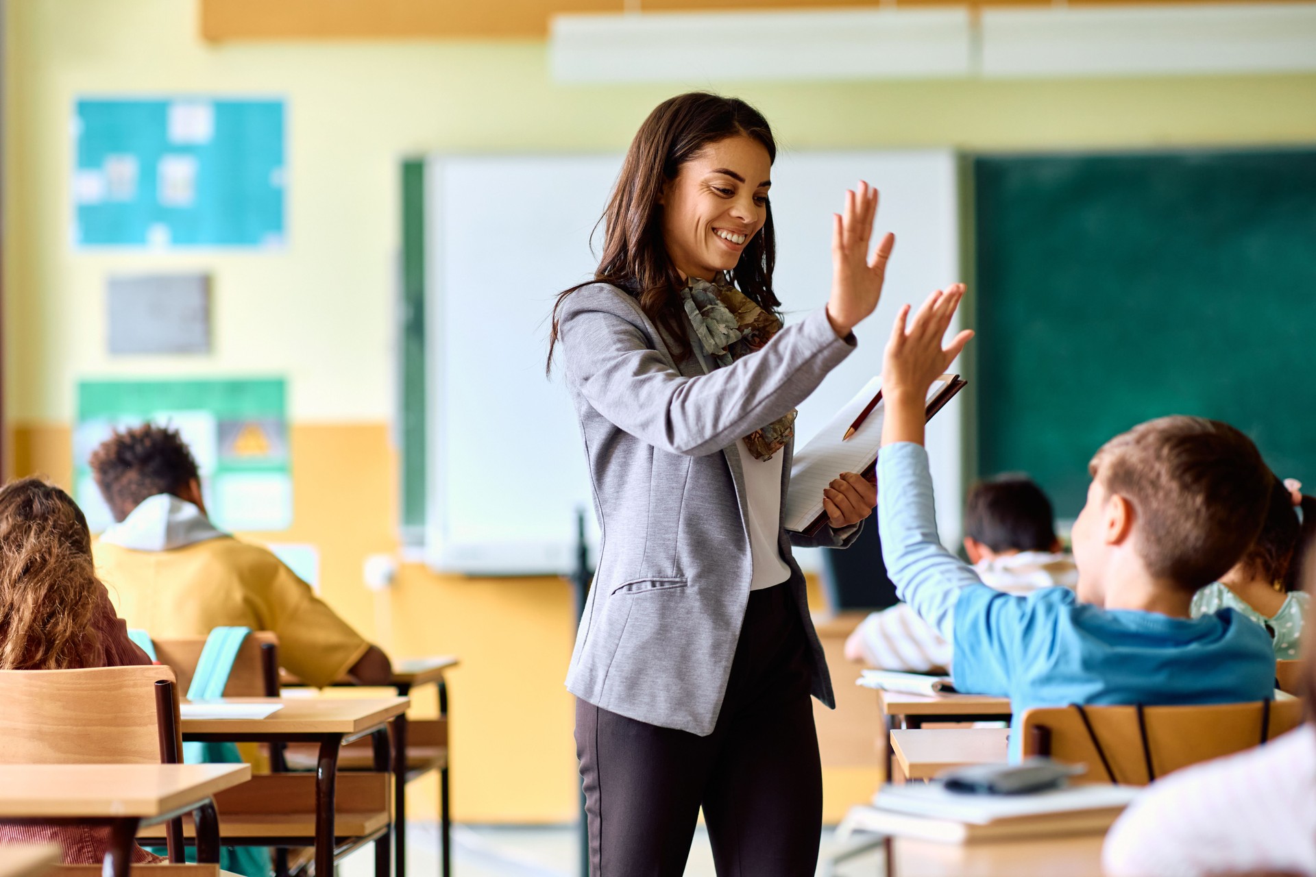 Happy elementary school teacher giving high-five to her student during class in the classroom.