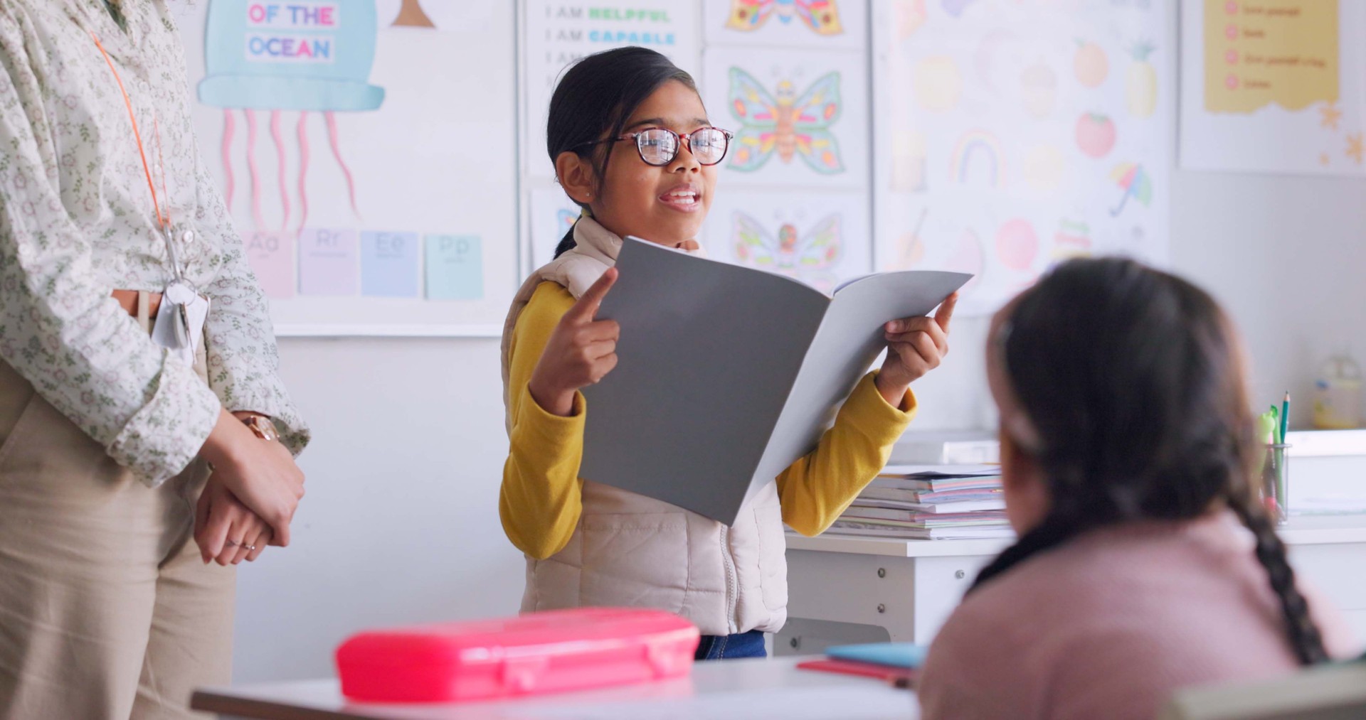 Child, reading and classroom with girl speaker, book and education at a school. Students, learning and notebook with development, knowledge and study work with story discussion of youth assessment