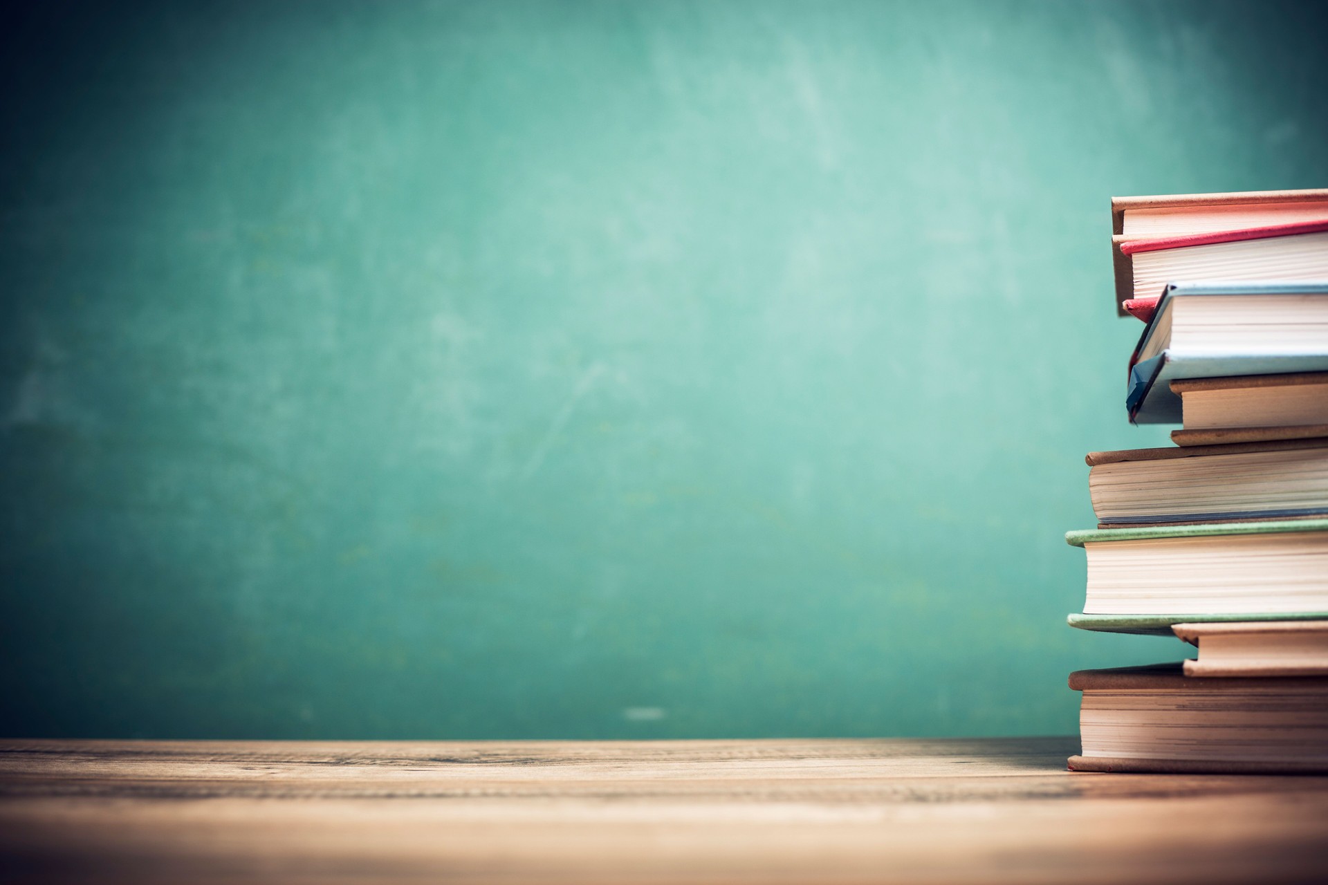 Textbooks on wooden school desk with chalkboard.